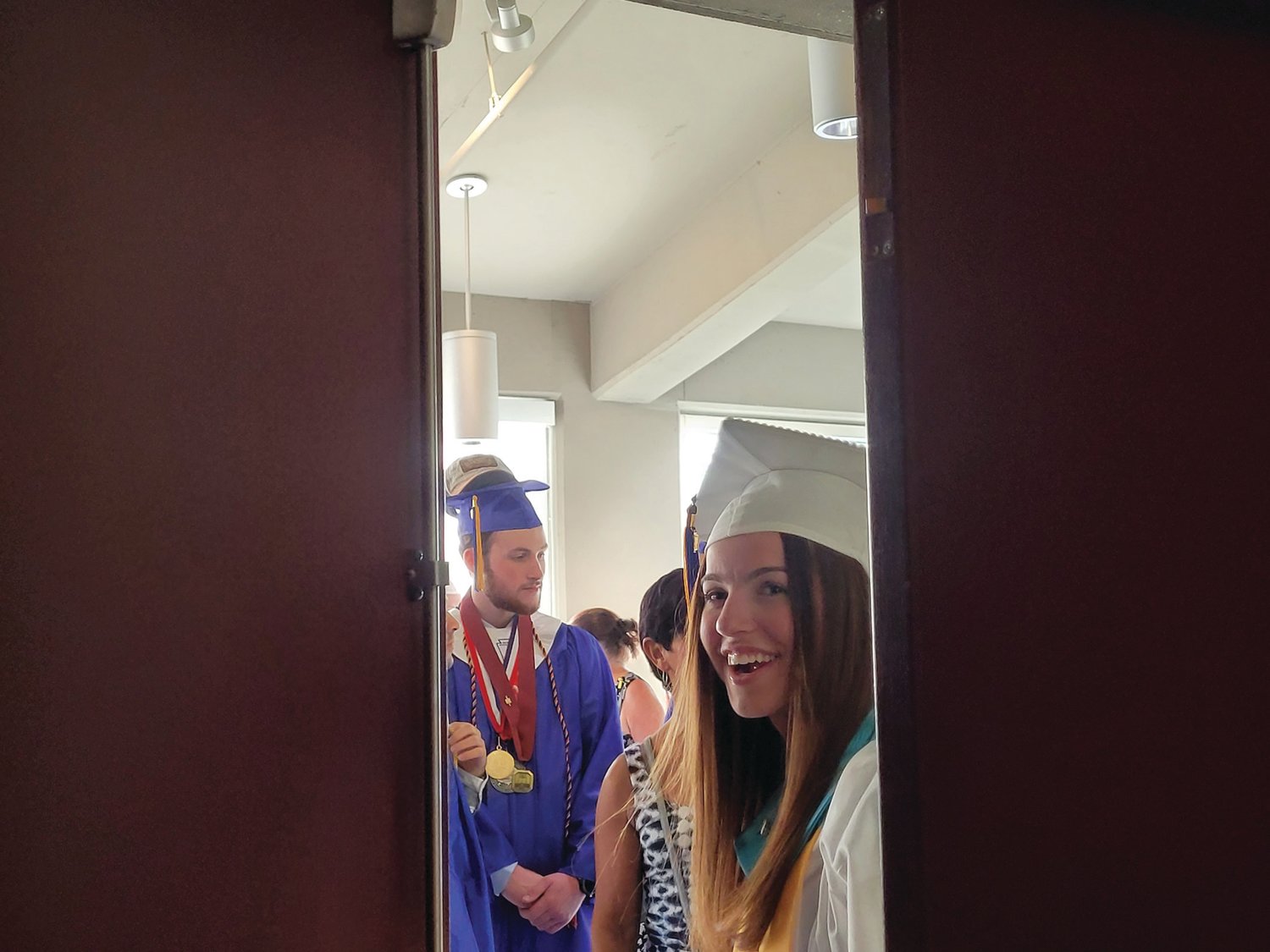 ANXIOUS GRADS: The Johnston Senior High School Class of 2022 lined up in a hallway behind the scenes of the ceremony held Friday at Veterans Memorial Auditorium in Providence. Students peaked through a doorway prior to their procession into the theater.